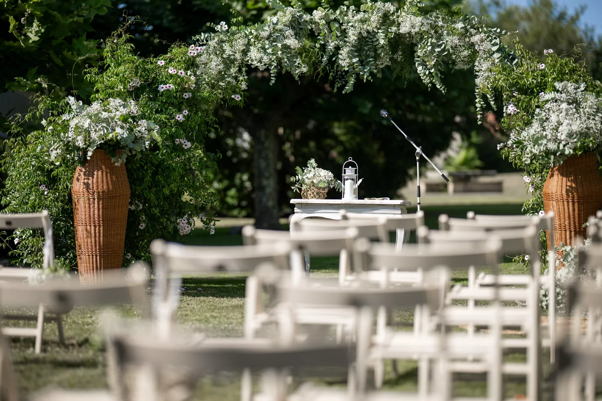 Sillas para invitados colocadas en un jardín frente a un altar con arco floral